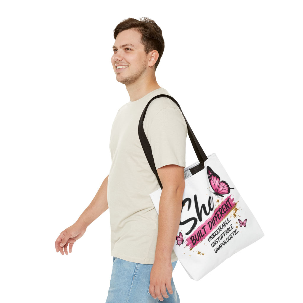 White tote bag with black handles on person, crown and pink butterfly “She Built Different”