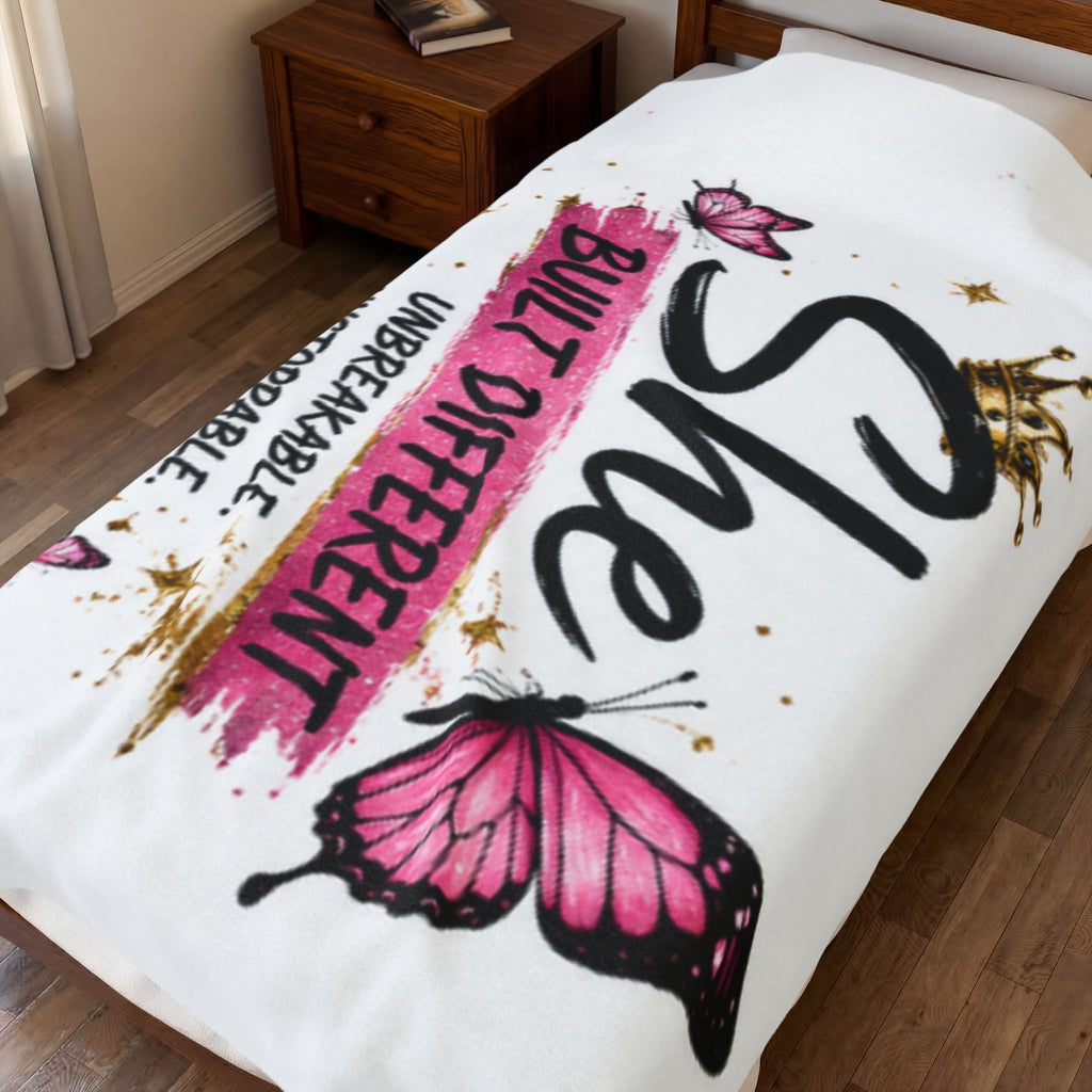 White plush blanket on bed with pink butterfly graphics and "Built Different" text
