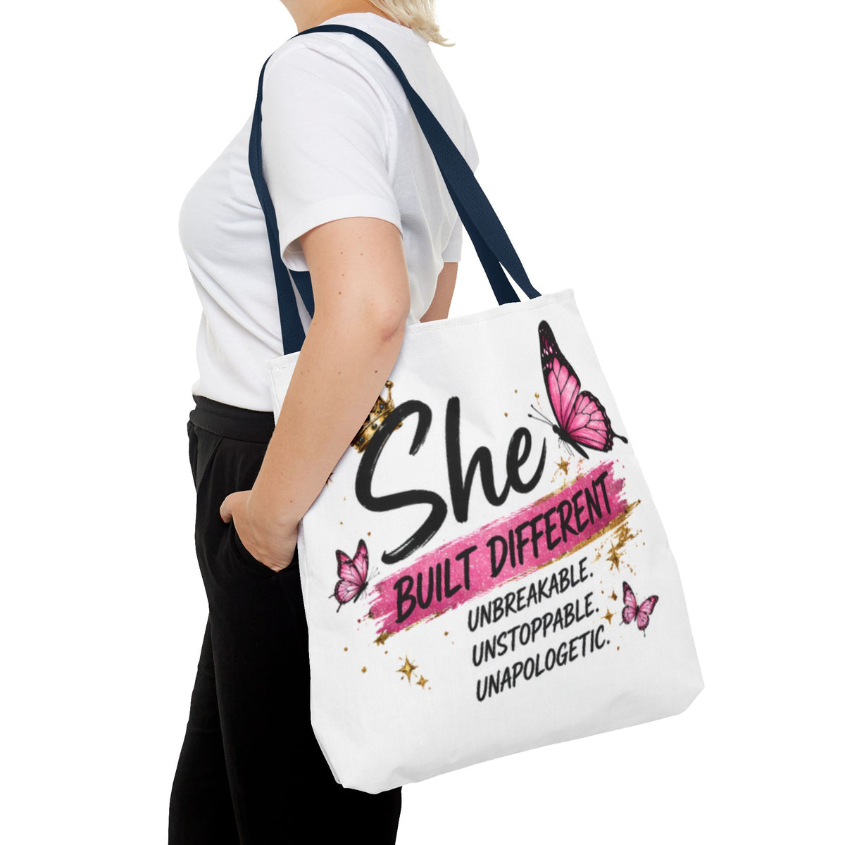 White tote bag with navy handles, pink butterfly graphic and “She built different” text