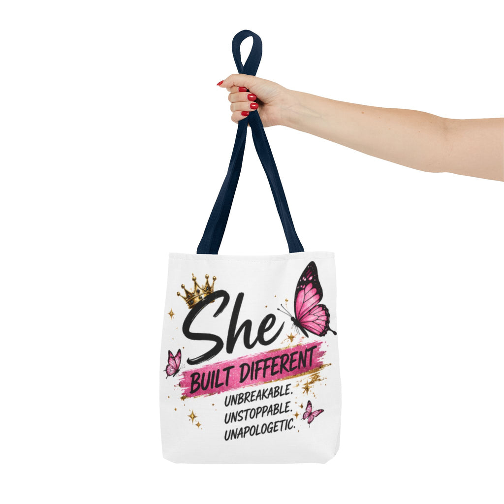 White tote bag with navy top handles, pink butterflies and “She built different” print