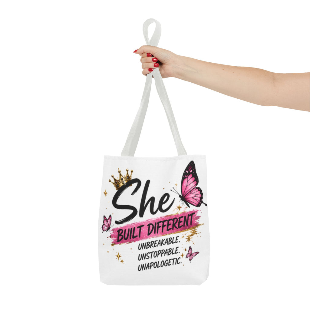 White tote bag with light gray handles, “She Built Different” butterfly graphic held up.