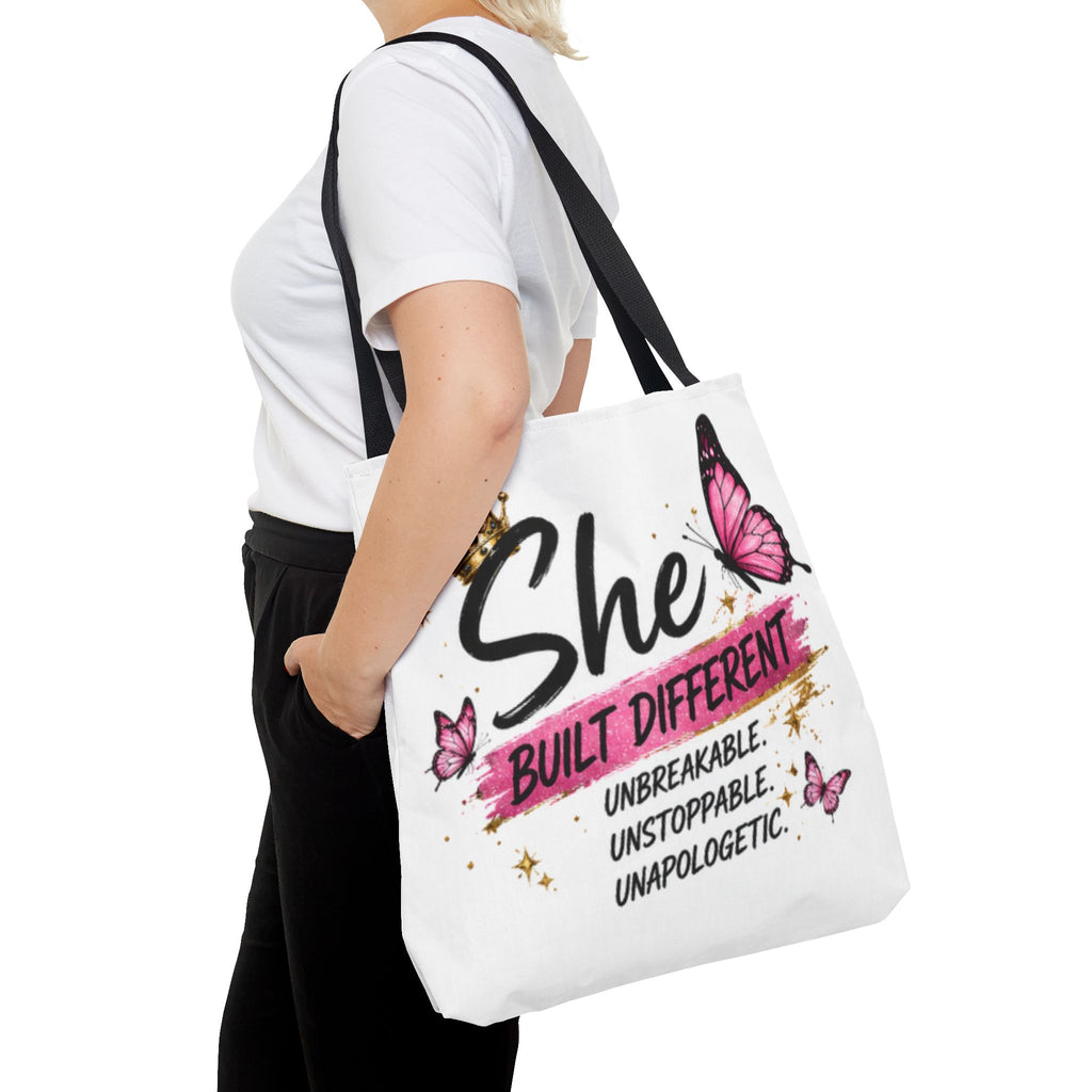 White tote bag with black strap and “She Built Different” slogan with pink butterflies