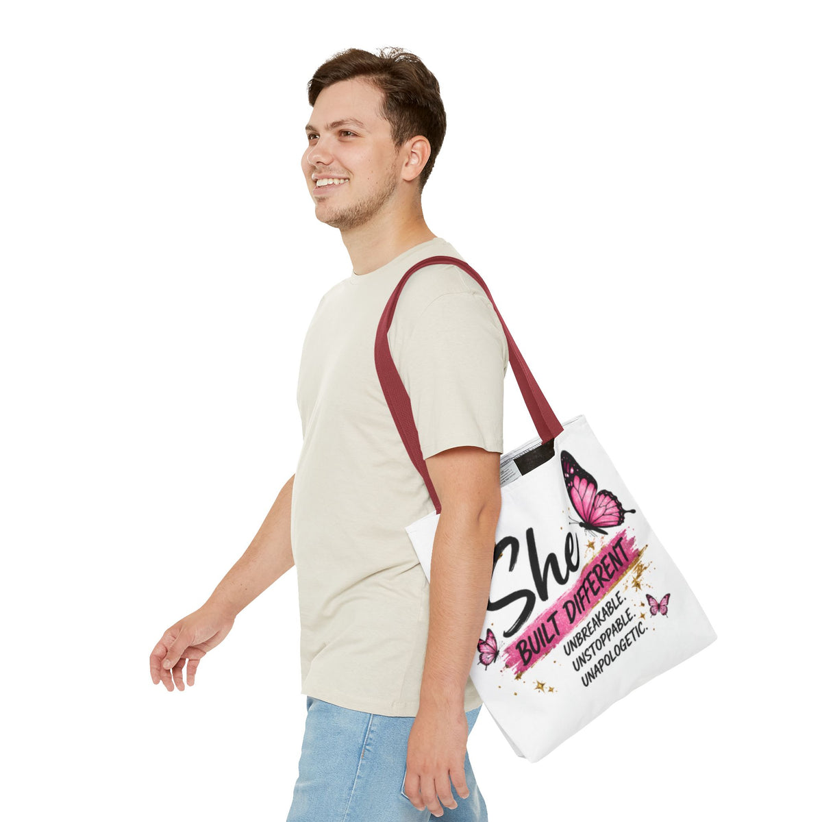 White tote bag with burgundy strap, “She Built Different” text and pink butterfly design